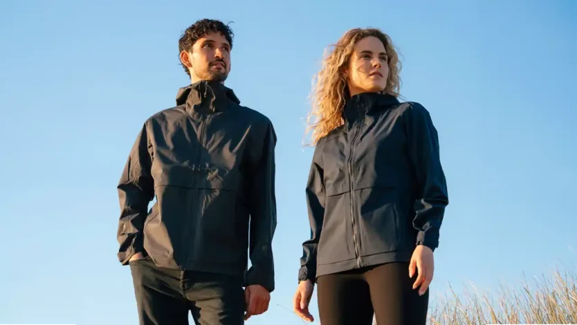 Man and woman wearing black performance jackets outdoors under a clear blue sky.